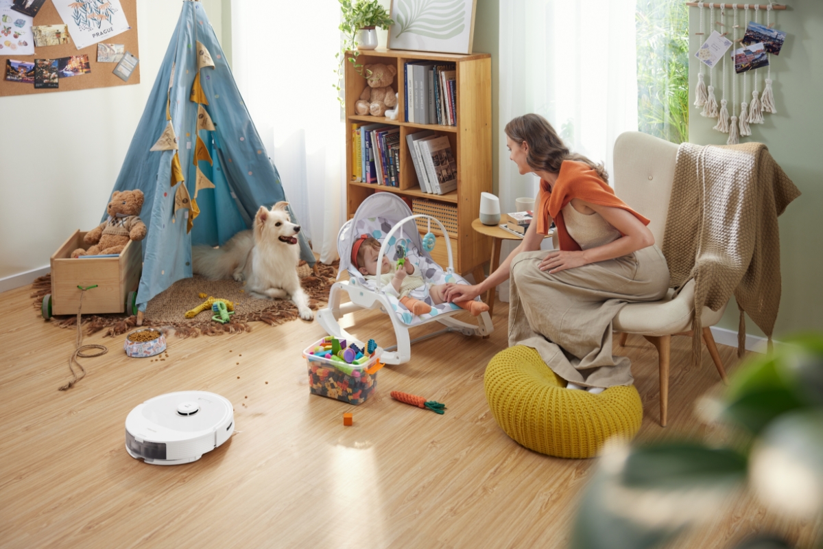 A parent looking after their baby on a sitter and their dog next to them, as the ROBOROCK Q8 MAX ROBOT VACUUM WHITE vacuums the floor next to them