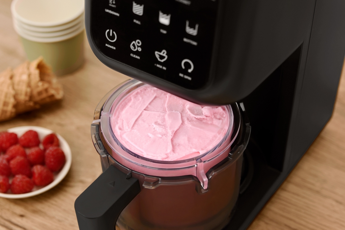 Black Point ice cream machine pictured a bit from above with its ice cream cup showing the pink ice cream inside the machine and some red berries on the wooden table next to the machine