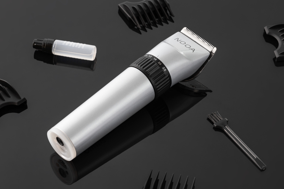 A silver-colored NOOA hair clipper placed on a shiny black table with all its accessories next to it