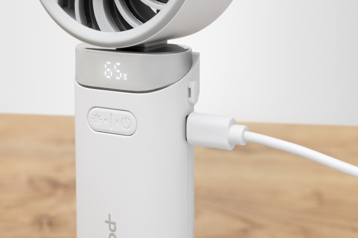 POINT HANDHELD FAN WH A white Point hand fan on a wooden table being charged with a white USB-C charging cable