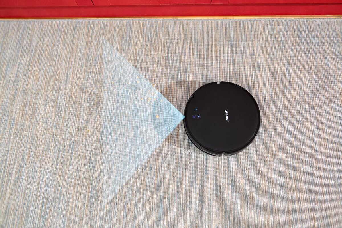 A picture of a black Point Dusty robot vacuum cleaner navigating on a grey floor with its infraded sensor scanning its surroundings