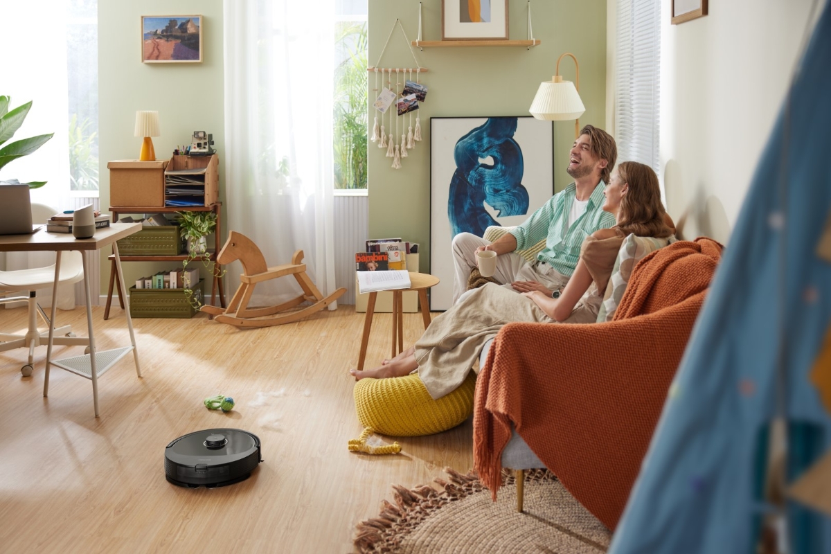 A couple laughing together on a sofa as ROBOROCK Q8 MAX ROBOT VACUUM BLACK vacuums the living room floor