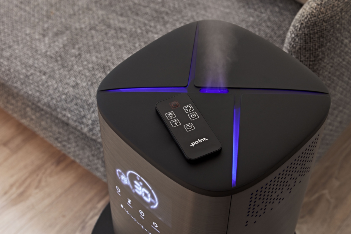 A close-up picture of a Point Pro Hydro humidifier and how it releases steam into the room air and its black remote control on top of the device