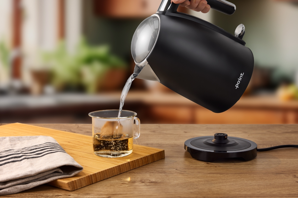 Wide angle image of a person pouring hot water from POINT POWK5020BK RETRO KETL BK/1,7/2200W into a glass tea cup, atop a wooden countertop