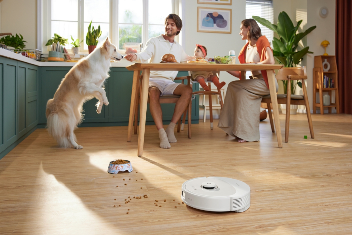 Wide angle image of a three person family and their dog around the dinner table, as the ROBOROCK Q8 MAX ROBOT VACUUM WHITE vacuums kibble off the floor