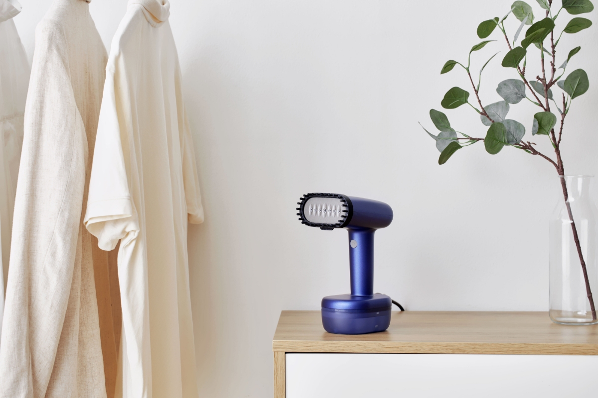 POINT PRO POHS15PRO STEAMER standing atop a wooden nightstand, with some white clothes on a clothing rail next to it