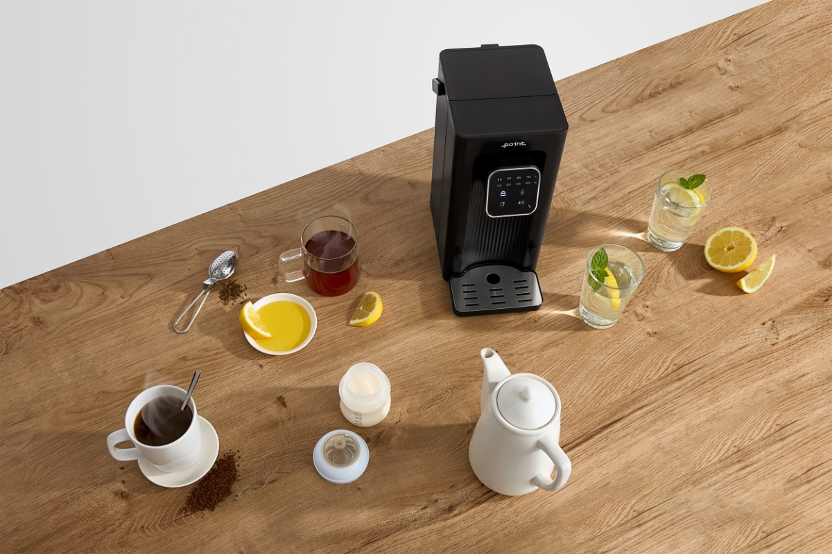 POINT POWD5000 INSTANT HOT WATER DISPENS A black Point hot water dispenser on a wooden table with several glasses of different teas and other drinks in see-through glasses around the machine