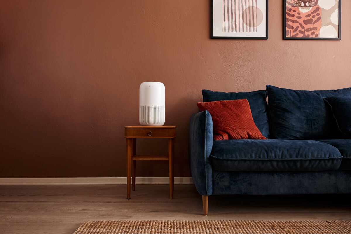 Air purifier on the side table next to a sofa and red wall with from a far