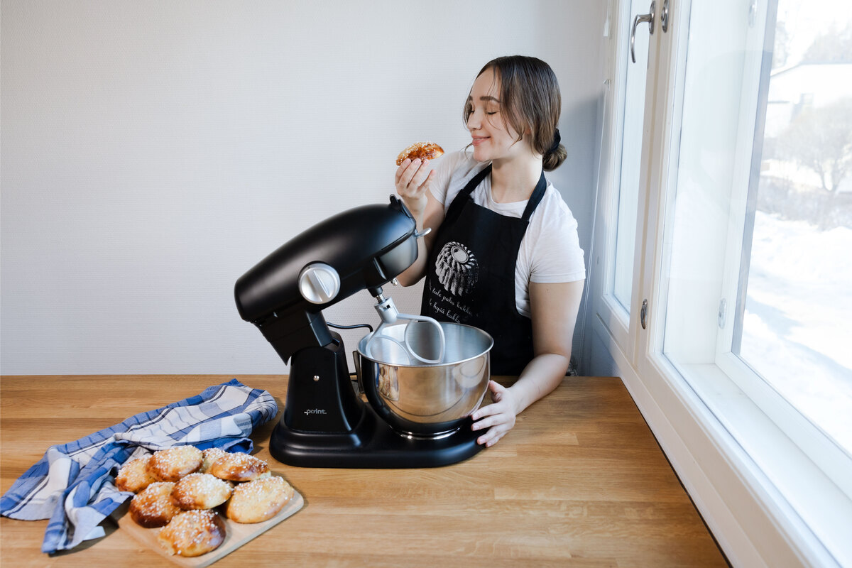 A woman baking with Point kitchen machine and eating fresh buns and buns on a wooden table