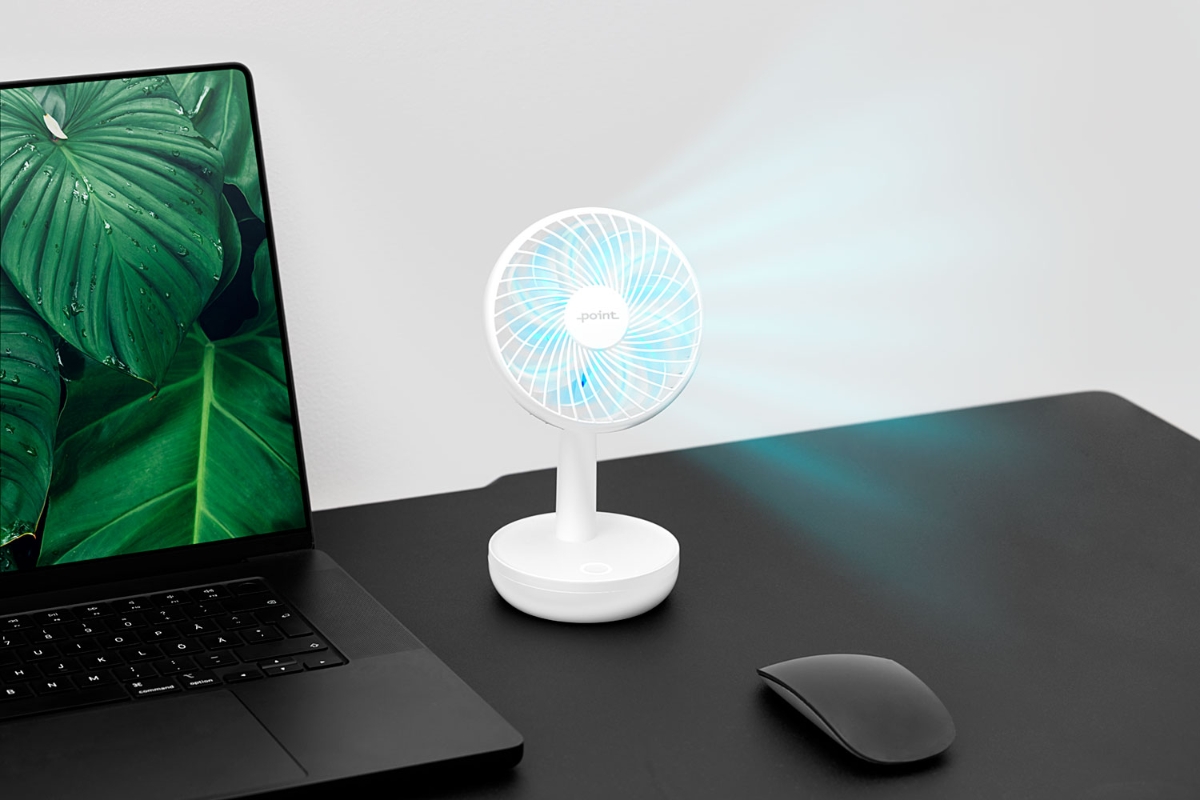 A white and small Point portable table fan on a black work desktop next to a black laptop and the fan blowing out air which looks blue thanks to the picture effects