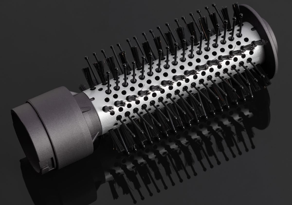 A silver and black colored brush attachment of the Nooa Allure air styler on a black shiny table