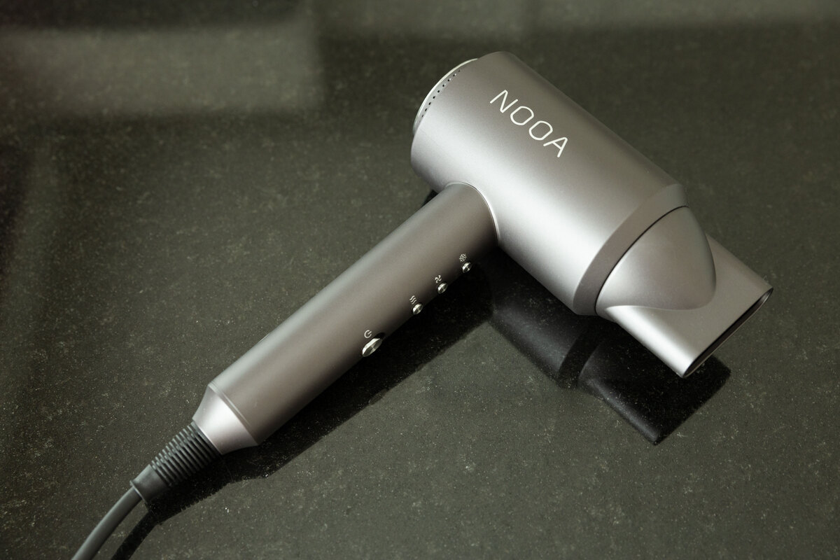 The NOOA LUXE BLDC hair dryer lying on a dark table