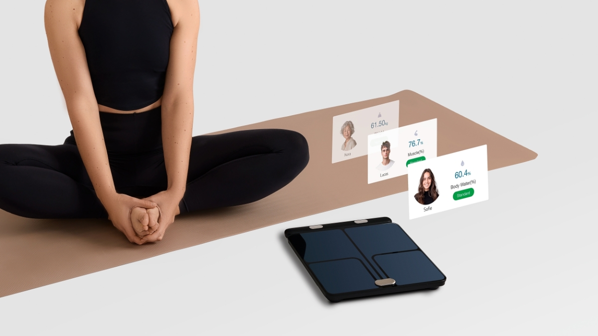 Close up of a person in black activewear sitting crosslegged on a beige yoga mat. NOOA Physiq in front of the mat with illustrations of the Moving Life app 