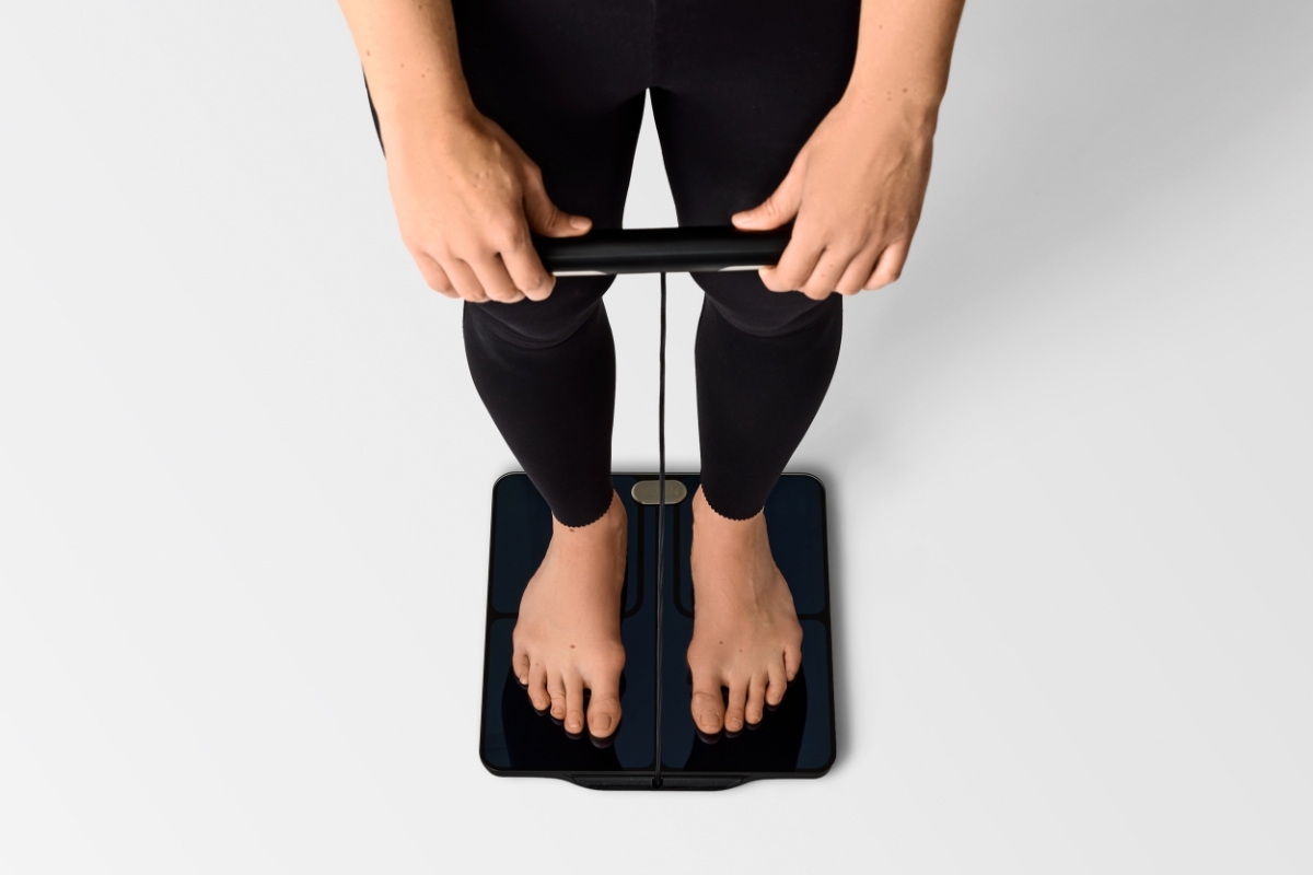 Birds eye view of a person in black active wear holding the handle of NOOA PHYSIQ SMART PERSONAL SCALE