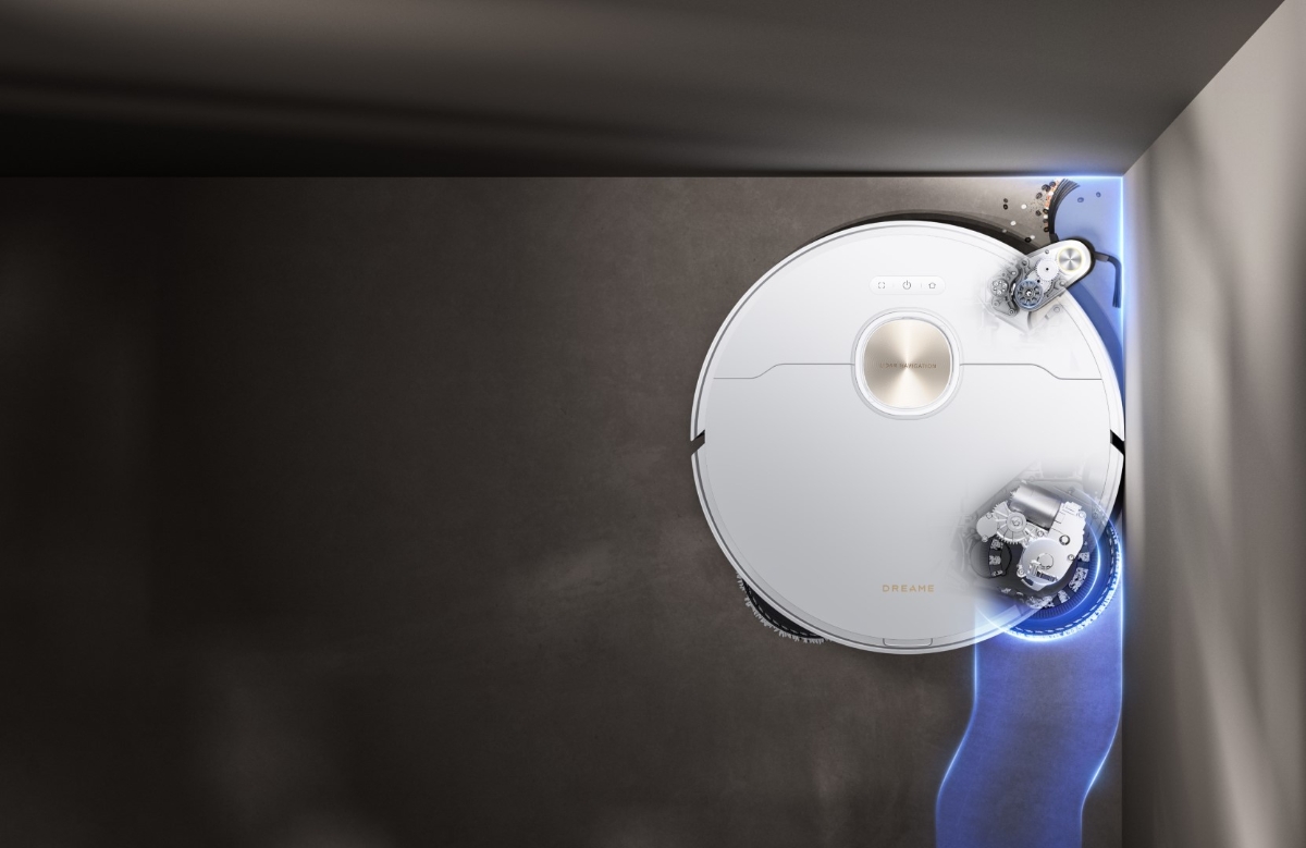 A white Dreame X40 Ultra robot vacuum cleaner on a dark grey floor vacuuming and mopping an edge of a grey wall and its side brush and mop pads reaching the corners of the wall