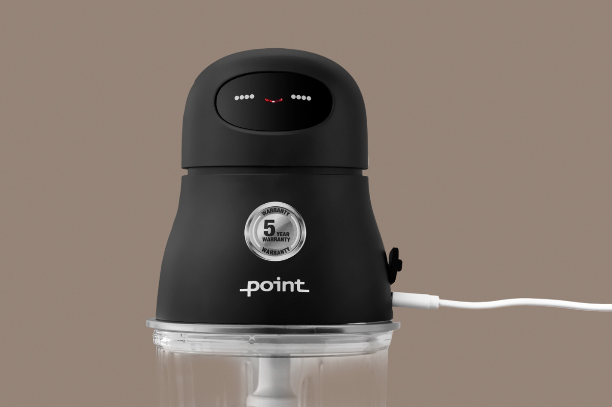 A close-up picture of a black Point cordless food chopper with a greyish background and a white USB-C charging cable attached to the side of the device