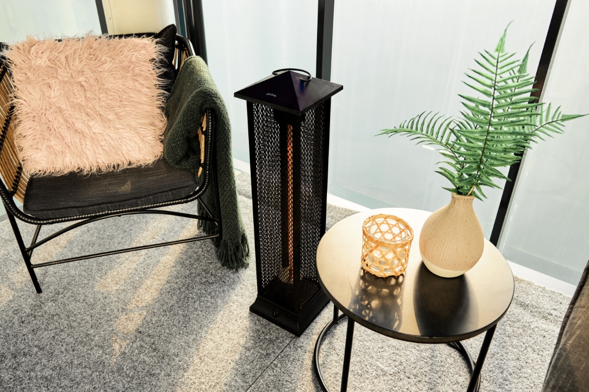A birds eye view of the POINT PRO POPHTOW81 patio heater. On the left to it is a lounge chair with pink throw pillow and a green blanket. On the right is a coffee table with a plant and a woven candle holder on it.