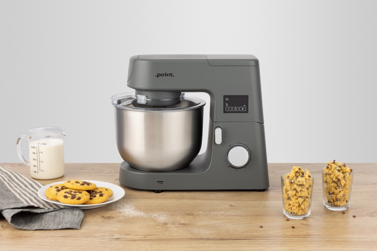 Grey-colored Point POKM5010 kitchen machine on a wooden table with ready-made chocolate chip cookies on a white plate and some cookie dough in transparent glasses and milk in a transparent cup