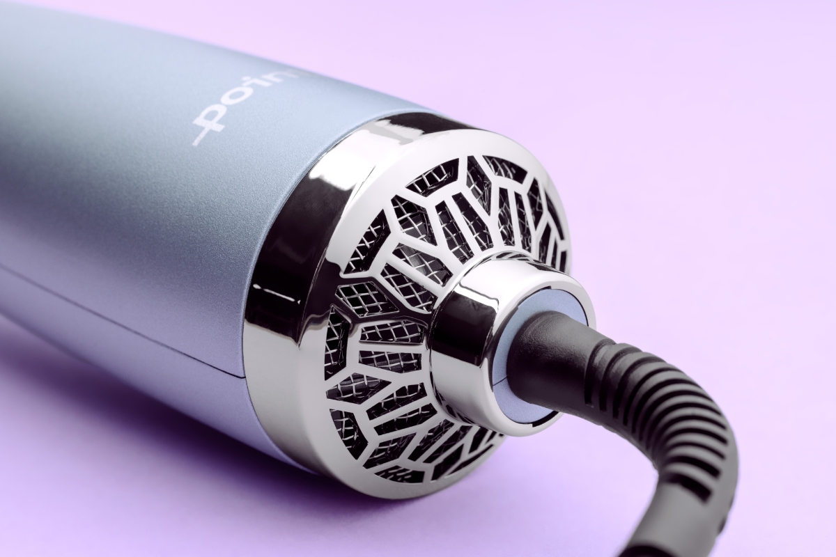 A close-up picture of a Point hot air brush's light-blue and silver handle with a black cord and a purple background