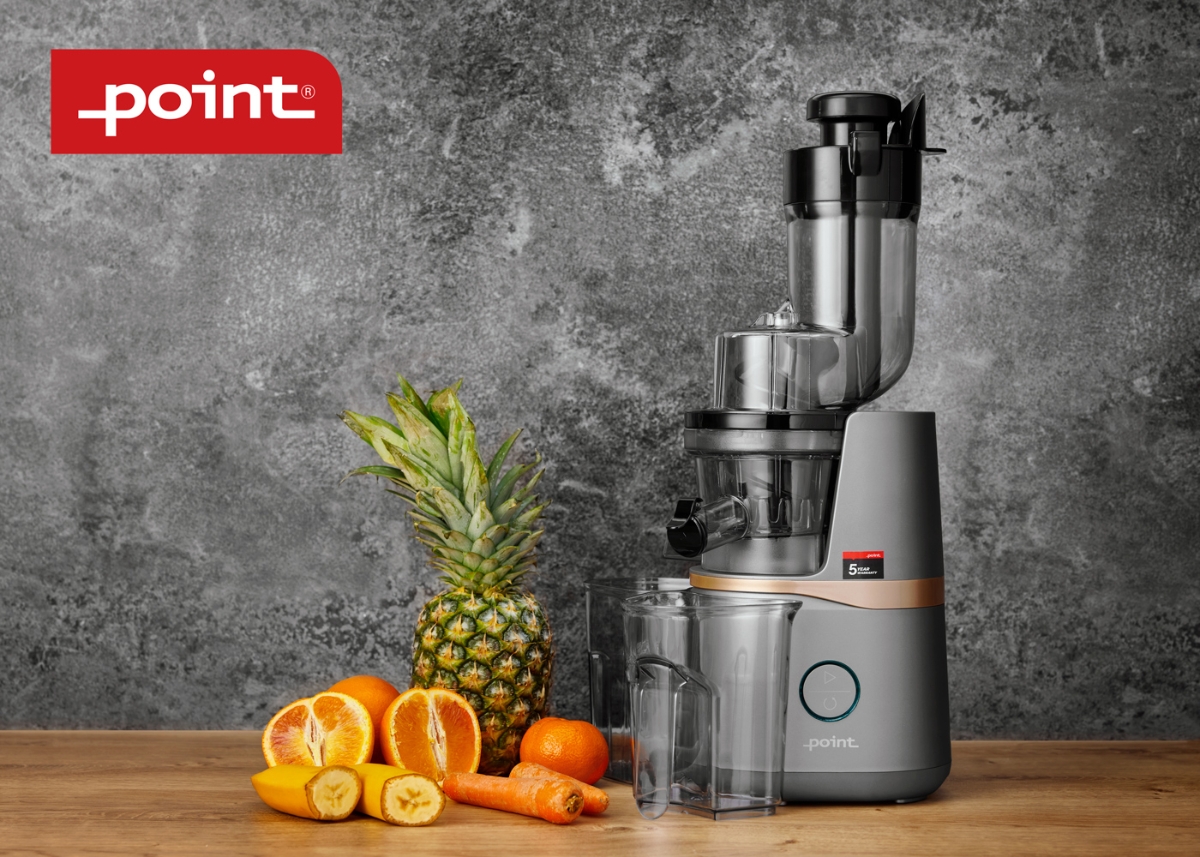 A grey-colored Point slowjuicer on a wooden table and a grey marble wall behind the device with orange and yellow fruits next to the device