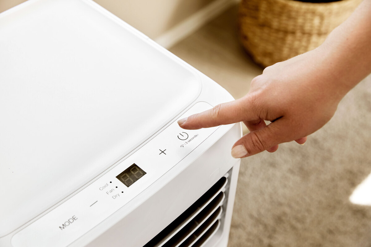 A close up of a person adjusting the settings of the POINT POAC6022 air conditioner on its touch control panel