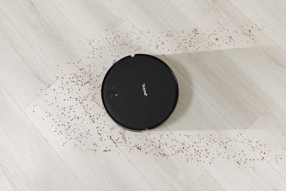 A black Point robotic vacuum cleaner mopping a light colored wood floor of crumbles