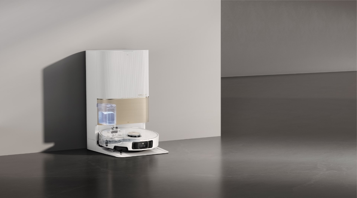 A white Dreame X40 Ultra robot vacuum cleaner in an empty room with grey shiny floors attached to its emptying station and the water tank of the station showing through the station