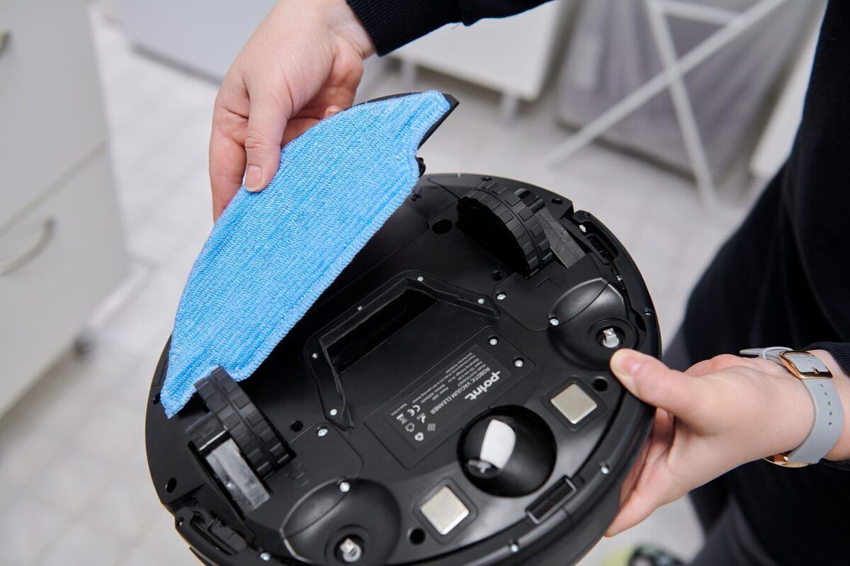 A picture of a black Point Dusty robot vacuum cleaner and it's blue mop cloth being attached to it's bottom in a white bathroom