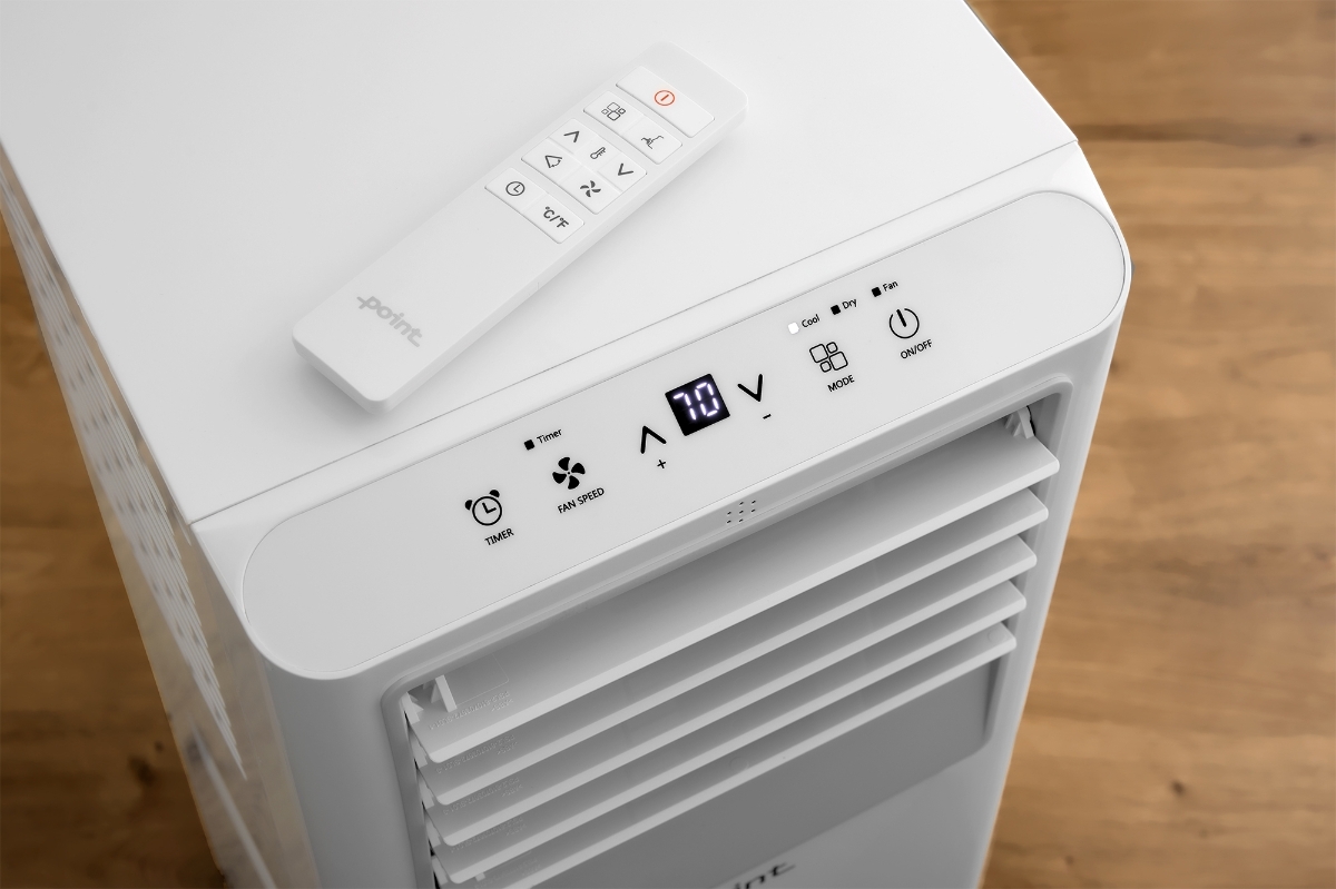 POINT POAC7K25 PORTABLE AC 7000BTU A white Point AC pictured from the bird view with its screen showing and a remote control on top of the device and a warm-toned wooden floor behind the device