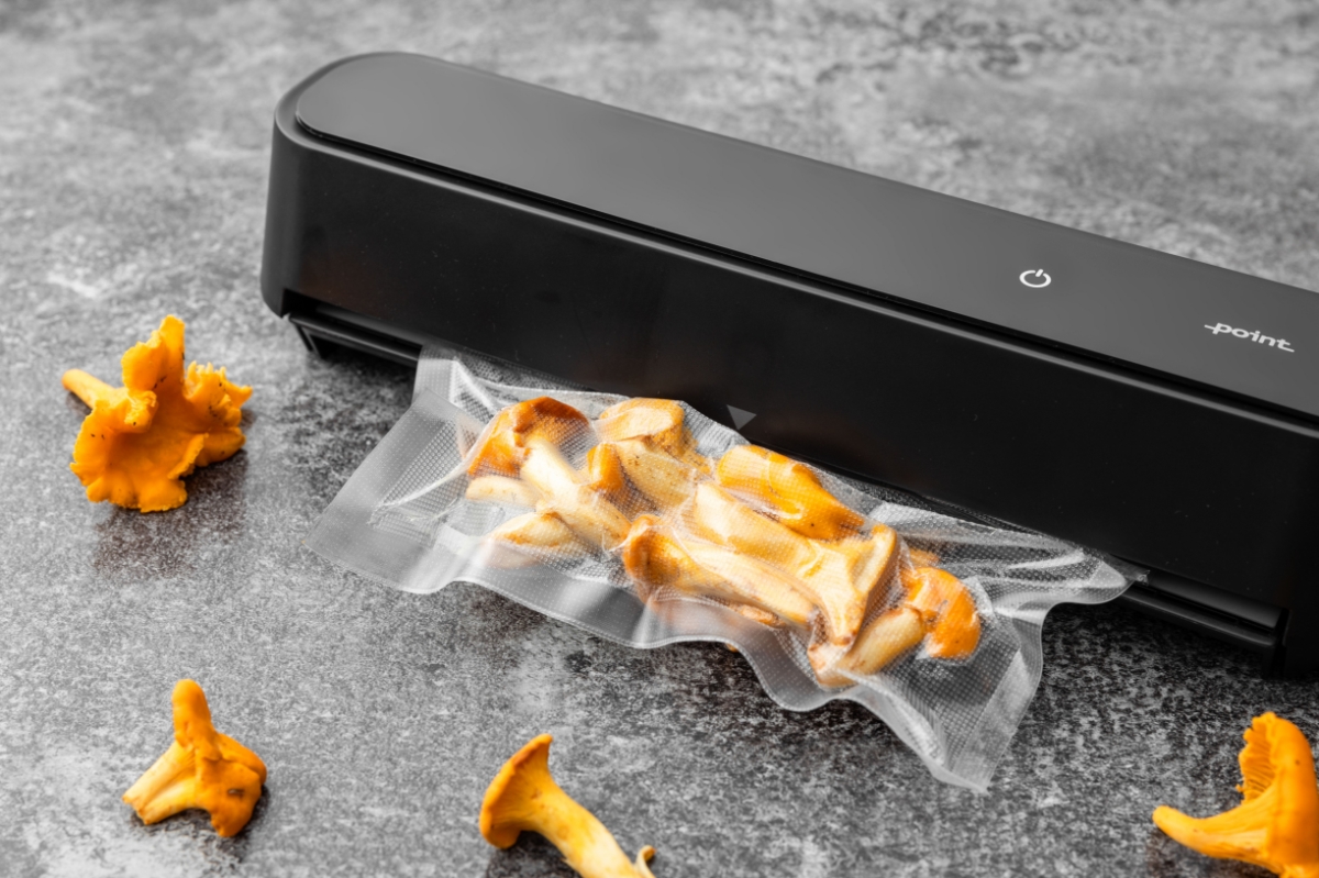 A close-up picture of a black Point vacuum sealer on a marble table with a vacuum bag full of yellow chanterelles next to it and chanterelles on the table also