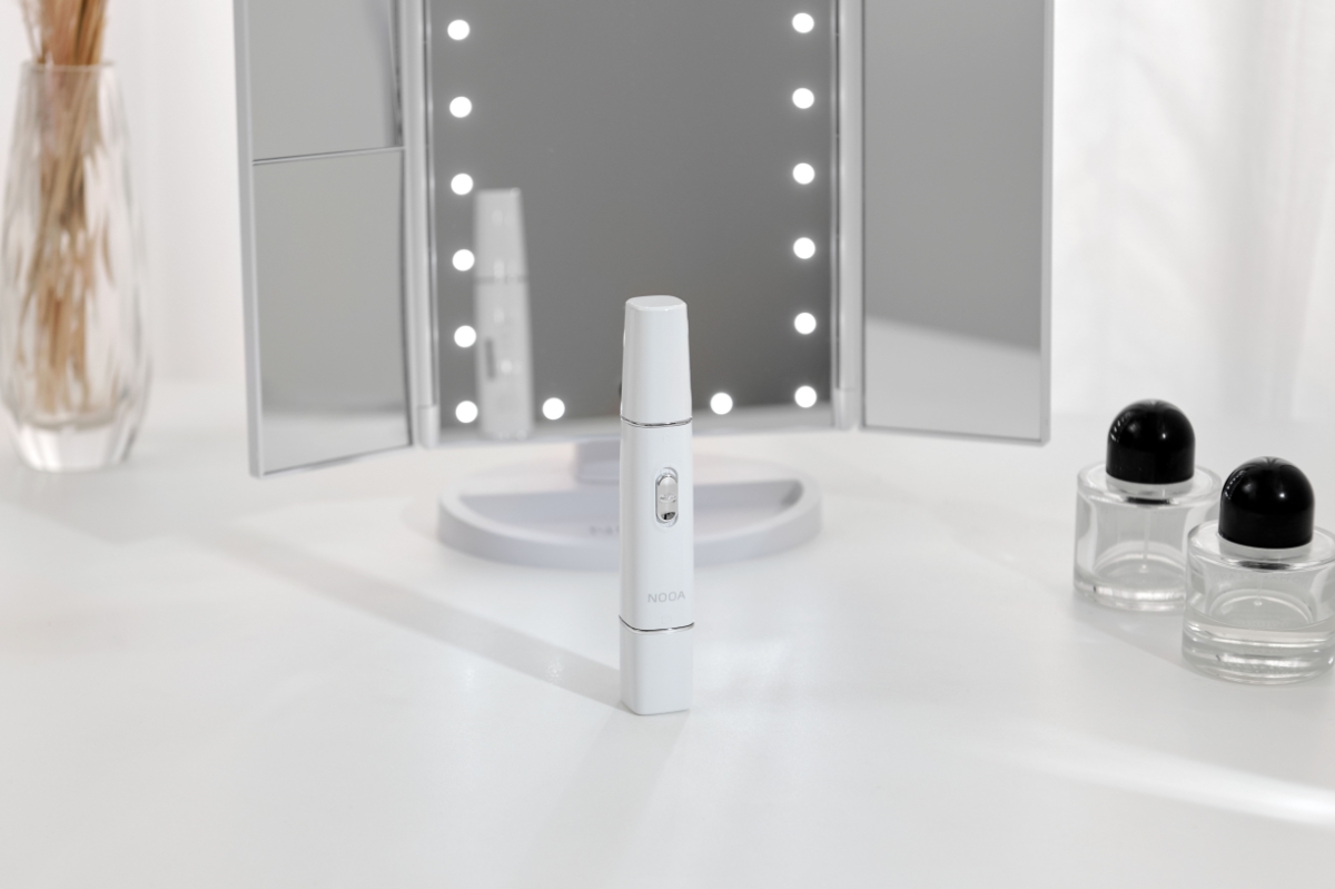 NOOA LISSE EYEBROW & FACIAL TRIMMER on a white table with the NOOA makeup mirror behind it