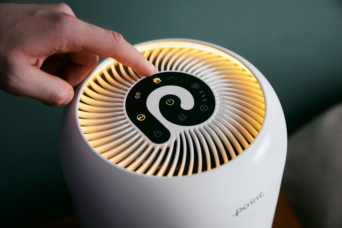 Person adjusting the air purifier by pushing the touch buttons on top of the device