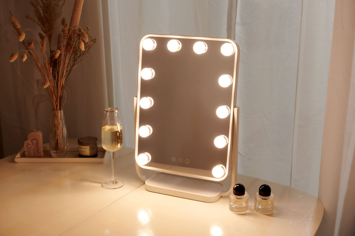 A picture of a NOOA makeup-mirror shining a warm light while standing on a white table with makeup-bottles next to it