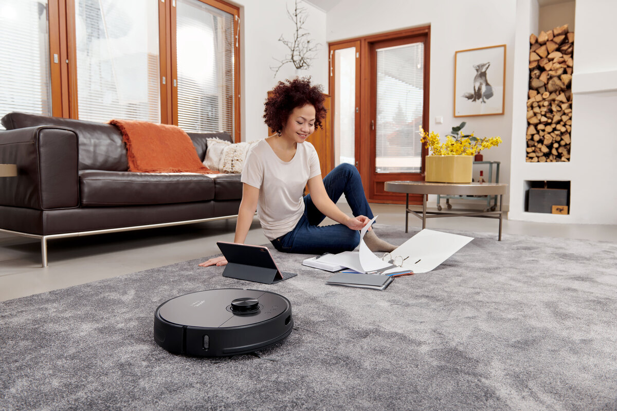 Woman working from home and robot vacuum next to her on the livingroom carpet