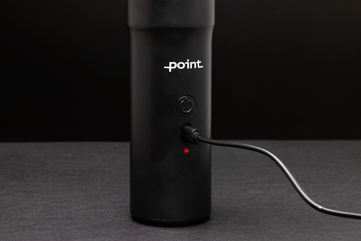 A black Point Tornado handheld vacuum cleaner pictured up close with a USB-C charger attached to the device and the device on a grey table and the background all black