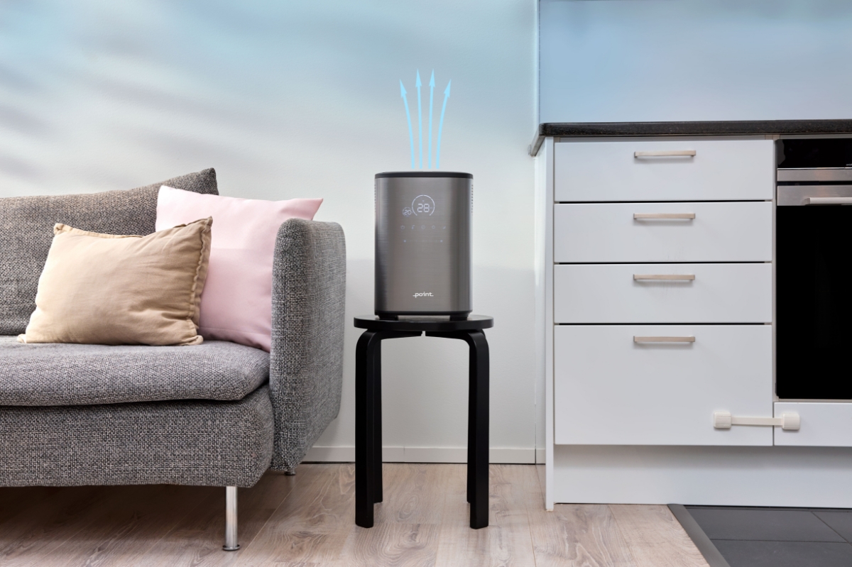 A picture of a Point Pro Hydro humidifier placed on a stool next to a grey couch and blue arrows point out of it showing the air vents
