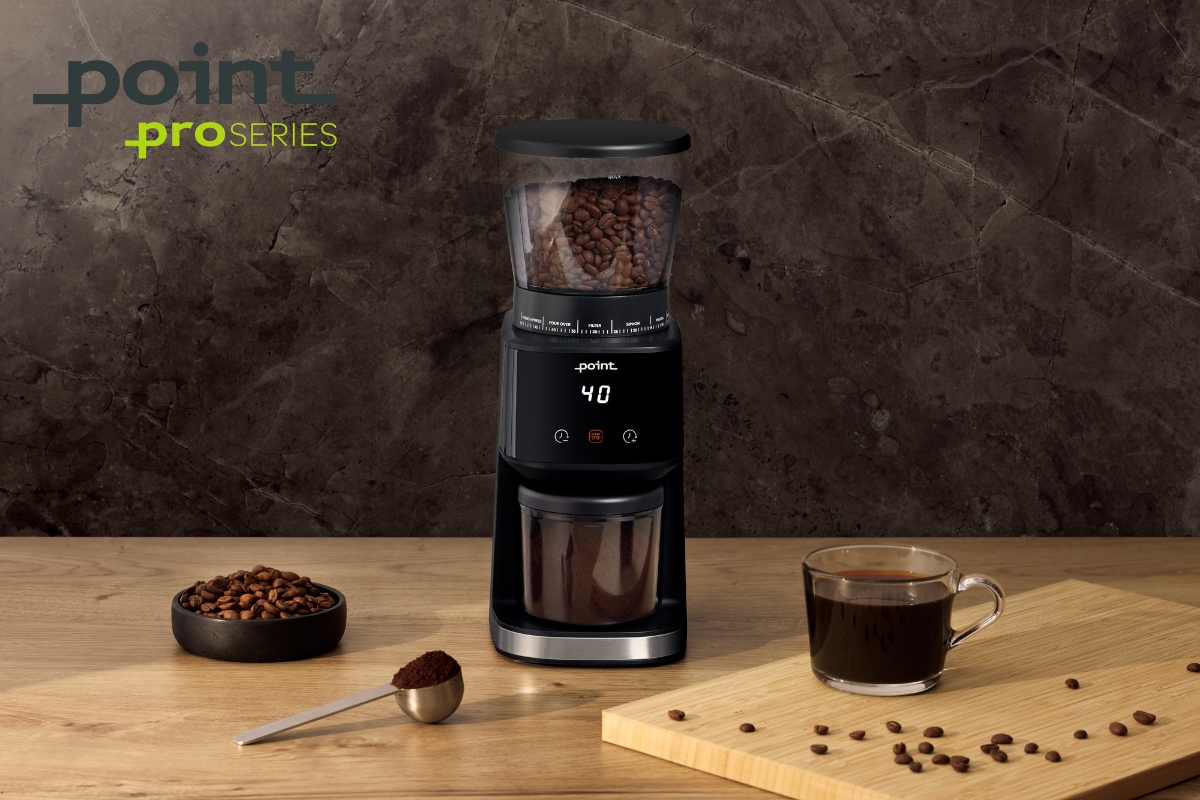 A black Point Pro coffee grinder on a wooden table next to some coffee beans on the table on a chopping board and on the table, a fresh cup of coffee in a glass mug and a Point Pro brand logo on the left up corner