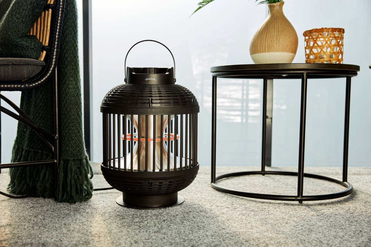Wide shot of the POINT PRO POPHLAN47 patio heater on a balcony floor, in between a lounge chair and a side table with a plant and a candle holder on it