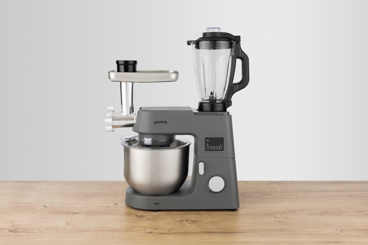 Grey-colored Point POKM5010 kitchen machine on a wooden table with the blender attachment attached to the top of the machine and the meat grinder attached to the left side and a light-grey background