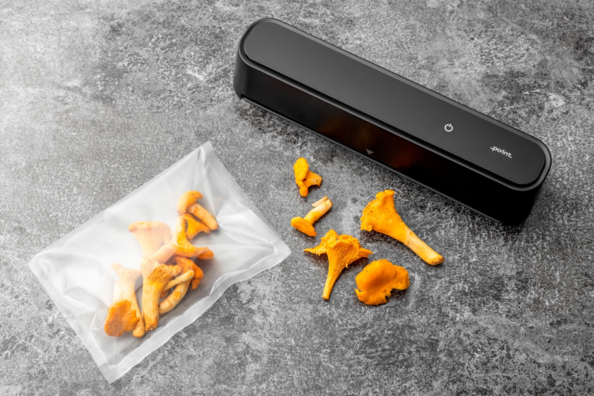 A picture of a black Point vacuum sealer on a marble table with a vacuum bag full of yellow chanterelles next to it and chanterelles on the table also