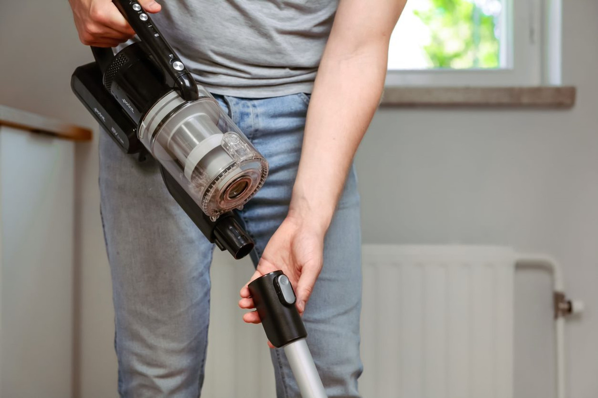 An image showing a person in grey t-shirt and blue jeans detaching the handheld vacuum from the POINT POVC618DB 18V stick vacuum